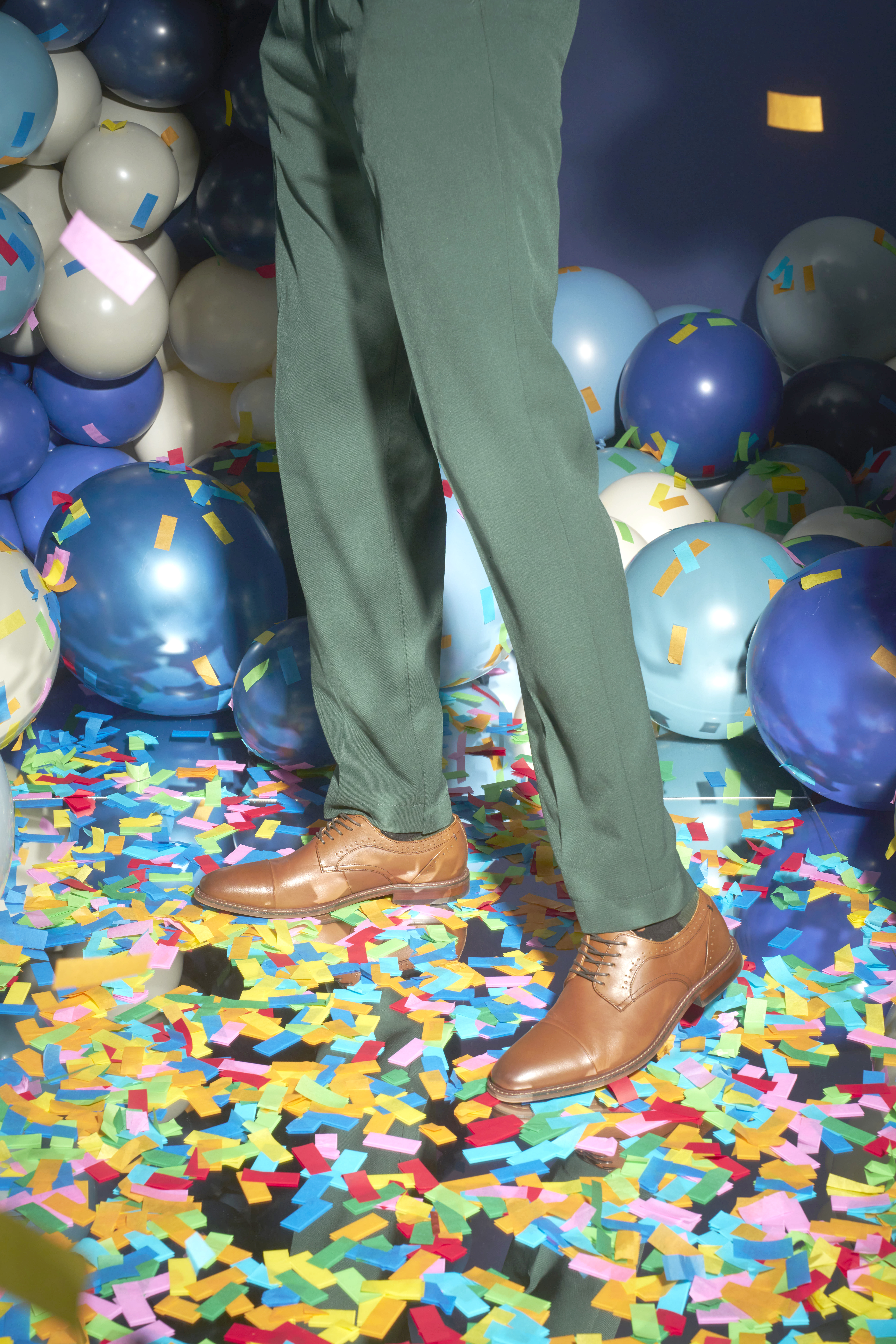 The featured image is a model wearing black Stacy Adams slip on shoes, black striped pants, and a white and black sweater while sitting on the floor with a blue abstract background.