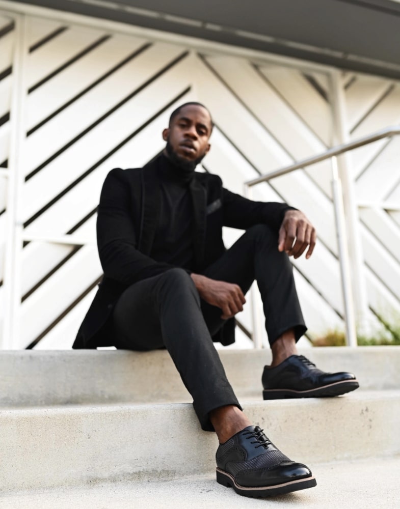 Image of social media influencer Chidi Ezemma sitting on steps while wearing the Callan Wingtip Oxford in Black.