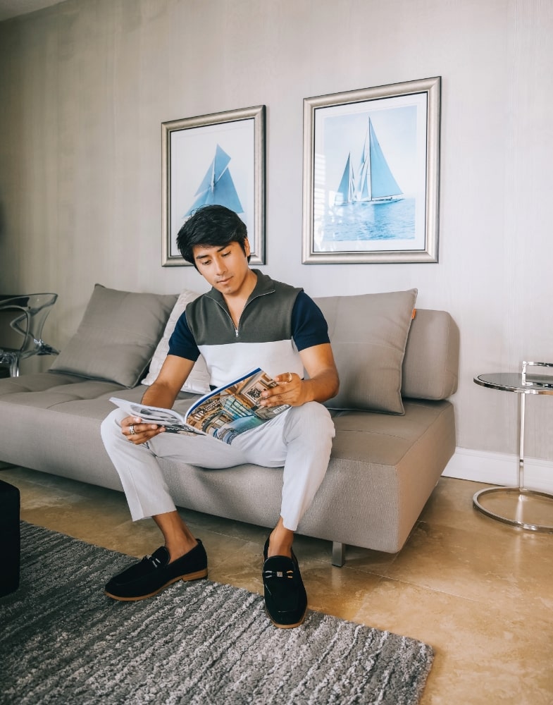 Image of social media influencer Marco Arrieta inside reading a magazine while wearing the Colbin Moc Toe Ornament Strap Slip On in Black Suede.