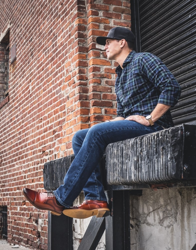 Image of social media influencer Mark from the duo "The NYC Couple" wearing the Dickinson Cap Toe Oxford in Cognac while sitting on a loading dock.