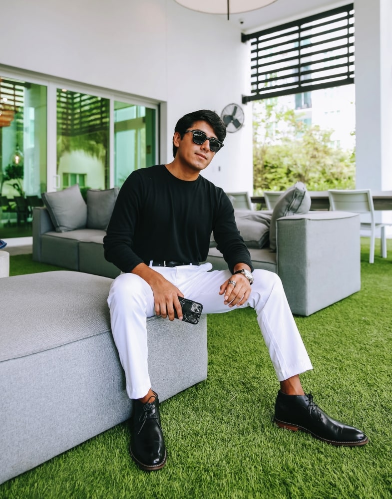 Image of social media influencer Marco Arrieta sitting on a couch wearing the Fraiser Plain Toe Chukka Boot in Black.