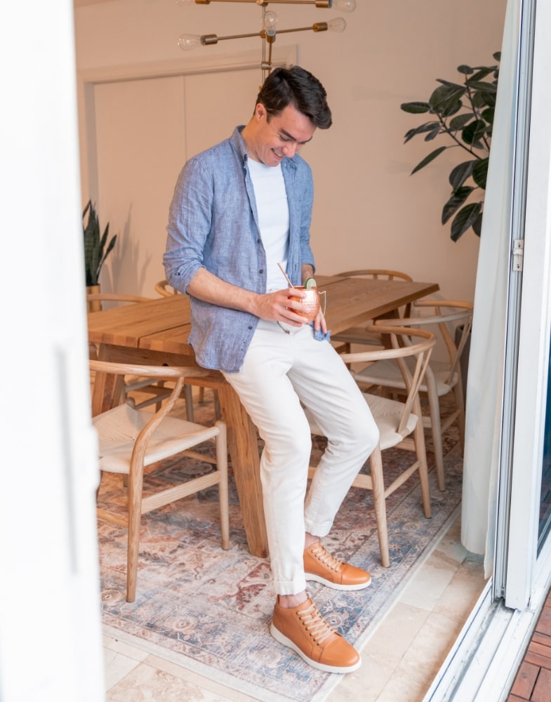 Image of social media influencer Alessandro Pontes standing against a table in the Harlow Cap Toe Mid Lace Up in Natural.