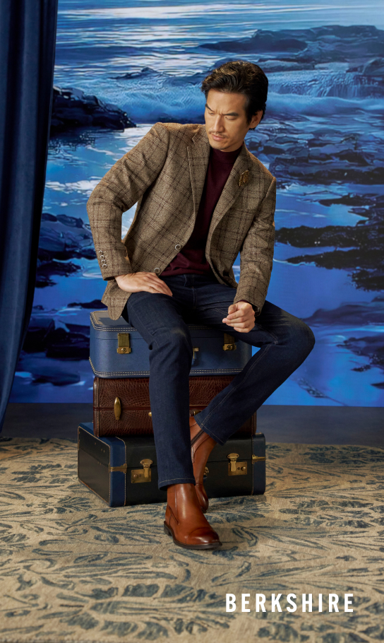 Men's Newest Shoes category Image features a mean wearing the Berkshire Cap Toe Side Zip Boot in Brandy sitting on suitcases.