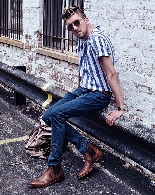 Image of social media influencer Thomas Trust wearing the M2 Wingtip Chelsea Boot in Cognac while sitting on a car railing.