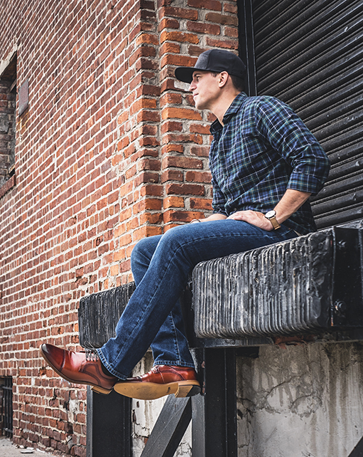 Image of social media influencer Mark from the duo "The NYC Couple" wearing the Dickinson Cap Toe Oxford in Cognac while sitting on a loading dock.
