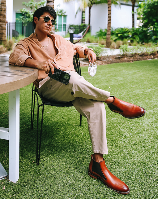 Image of social media influencer Marco Arrieta sitting at a table outside wearing the Fabian Plain Toe Chelsea Boot in Cognac.